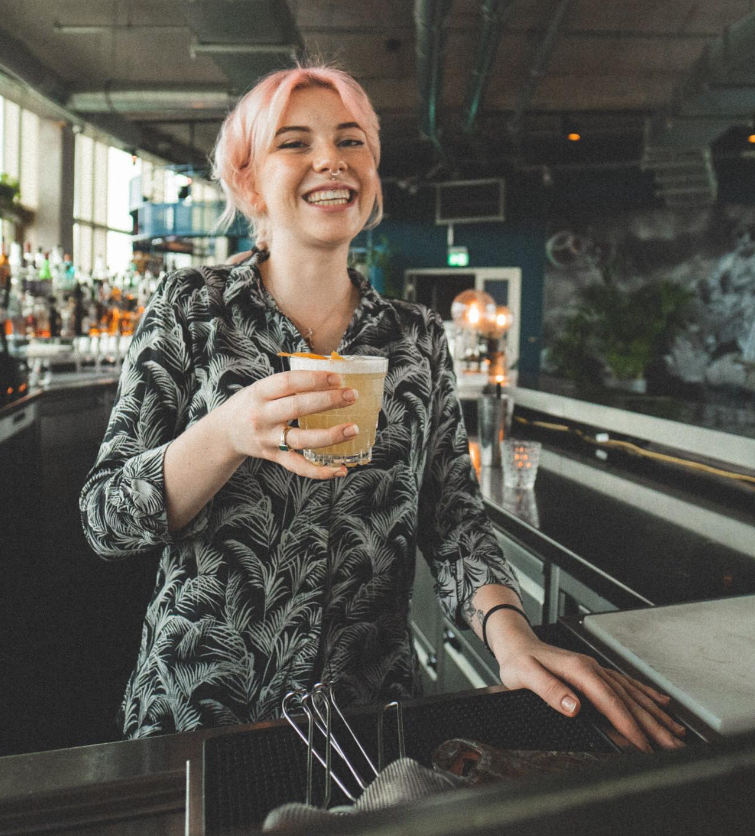 A bartender in the Monkey Bar uniform holding a drink and smiling